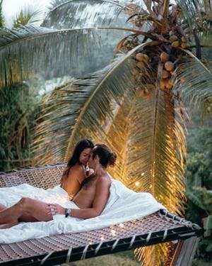 couple laying on a net surrounded with fairy lights and a palm tree in the back. Camaya Bali, photo by @pilianddano