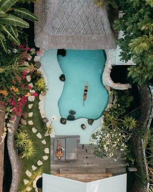 Drone shot of a couple in a villa with a pool. Man laying in a sun bed and woman floating in the pool. Kuno villas, photo by @pilianddano