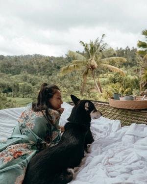 woman and a black dog laying in a nest bed in bali looking towards the ricefields