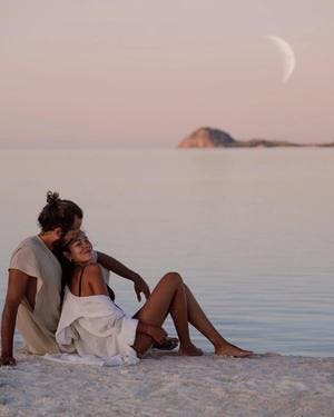 Dano kissing Pili in her forehead at the beach with the ocean and the moon in the back. Komodo Island, photo by @pilianddano